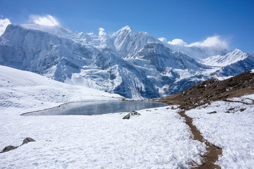 Fototapeta na wymiar A tranquil mountain lake lies nestled among snow-covered peaks, reflecting the grandeur of the towering Himalayas under a clear sky.
