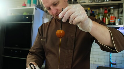 Man in latex gloves keeps candy stick in caramel with hand. Chef plunges candy into caramel waiting...