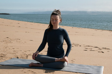 Fototapeta na wymiar Young woman practicing yoga on the beach by the sea. Healthy lifestyle concept.