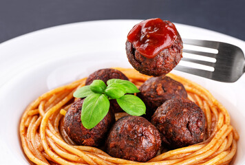 Fried vegan meatballs with noodles and basil leaves on a plate. Fork with a meatball and ketchup.