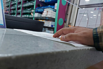 Man at medicine counter holding prescription in hand.
