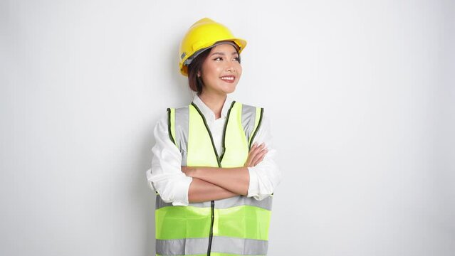Smiling Asian woman labor worker in industry factory, posing with arms folded, wearing yellow safety helmet, green vest and uniform, isolated white background.