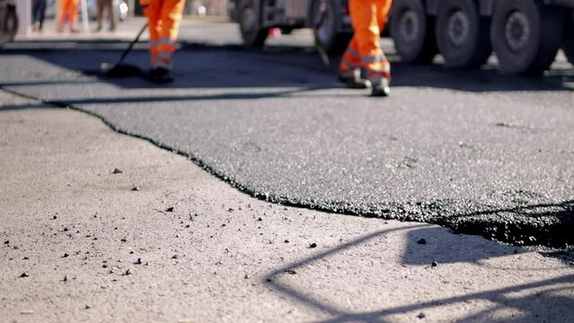 Steam rises from the hot asphalt surface. A worker levels fresh asphalt at a construction site.