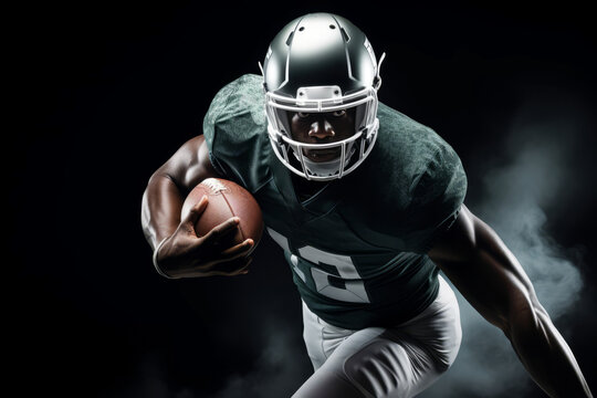 Portrait of American football player running with the ball. Muscular African American athlete in a green and white uniform with an ovoid ball in a dynamic pose. Isolated on black background.