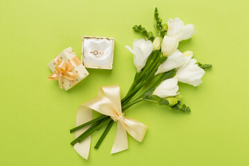 Fototapeta na wymiar White freesia flower and gift box with diamond ring on color background, top view