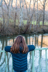 a girl looks at the river from a bridge leaning against a fence, with her back to the river