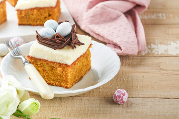 Easter carrot cake bars decorated with chocolate nest and chocolate candy eggs blossoming cherry or apple flowers on rustic light wooden backgrounds. Easter holiday meal. Traditional Easter food.