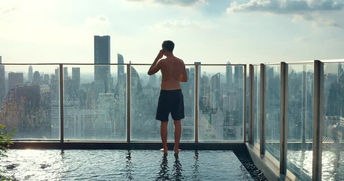 Man stands on rooftop with pool in nice luxury hotel mesmerized by cityscape Rooftop with pool offers luxurious freedom. From rooftop with pool panoramic view of the metropolis unfolds.