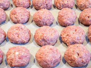 Delicious rolled meatballs on a baking plate with parchment paper, ready for the first bake in the oven before frying.