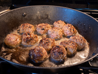 Closeup view of golden brown meatballs frying in butter in a frying pan.