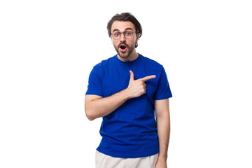 young smart caucasian man with dark well-groomed hair and beard in a blue t-shirt points his hand to the side with copy space