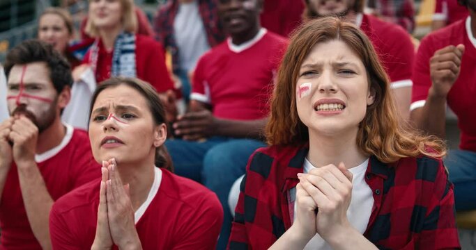 Beautiful Caucasian girls with painted faces worrying while watching fierce football game. Happy fans giving each other high fives and rejoicing over goal scored in opponent's net.