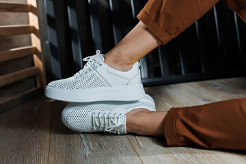 Close-up of female legs in white perforated leather sneakers. Women's summer sneakers. Collection...