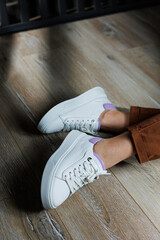 Comfortable female legs in white sneakers with flat soles. Close-up of female legs in leather...