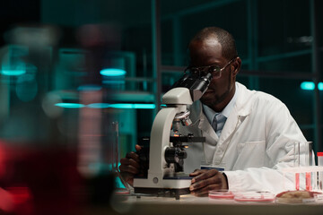 African american scientist sitting at his workplace in laboratory working with microscope