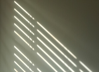 Sunlight shining through window blinds and casting a shadow on an interior wall.