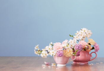 beautiful spring flowers in two cups in pastel colors on blue background