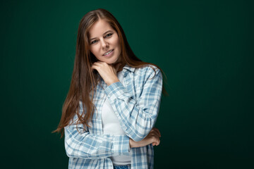 Confident Caucasian young woman stands in a leader's pose on a green studio background