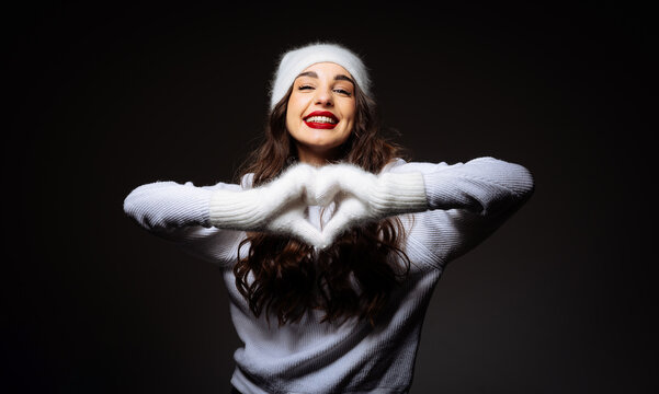 A Woman in a White Hat and Sweater Making a Heart With Her Hands
