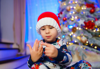 A Joyful Little Boy in Front of a Festive Christmas Tree. A little boy sitting in front of a...