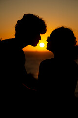 Young couple, in silhouette, with the sun in the background.