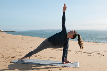 Full length portrait of young woman practicing yoga on mat at seaside
