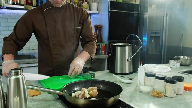 Chef places garlic slices into skillet alongside frying meat cubes. Beef cubes imbibe unique taste arising from combination of garlic and spices