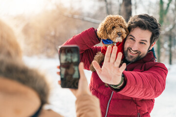 Happy smiling man waving hand at the camera posing for a photo with a dog while a woman is...