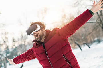 Excited mid adult man testing virtual reality glasses having fun outdoors on winter day in city...