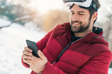 Closeup of smiling adult man using mobile phone while wearing virtual reality goggles outdoors.