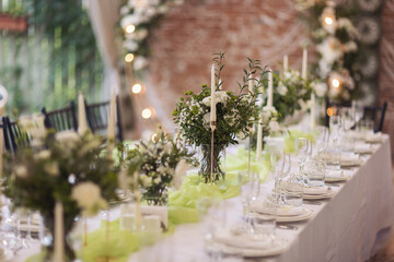 Stylish elegant table setting for festive dinner. The chairs and table for guests, served with cutlery, greenery flowers and crockery and covered with a white tablecloth. Catering on Wedding. Banquet.