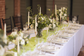 Stylish elegant table setting for festive dinner. The chairs and table for guests, served with cutlery, greenery flowers and crockery and covered with a white tablecloth. Catering on Wedding. Banquet.