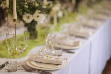 Stylish elegant table setting for festive dinner. The chairs and table for guests, served with cutlery, greenery flowers and crockery and covered with a white tablecloth. Catering on Wedding. Banquet.