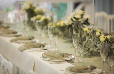 Stylish elegant table setting for festive dinner. The chairs and table for guests, served with cutlery, greenery flowers and crockery and covered with a white tablecloth. Catering on Wedding. Banquet.