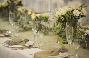 Stylish elegant table setting for festive dinner. The chairs and table for guests, served with cutlery, greenery flowers and crockery and covered with a white tablecloth. Catering on Wedding. Banquet.