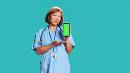 Clinic employee showing medical instructions video on phone green screen. Asian nurse wearing...