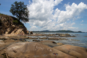Rocky shore with scattered boulders under a partly cloudy sky