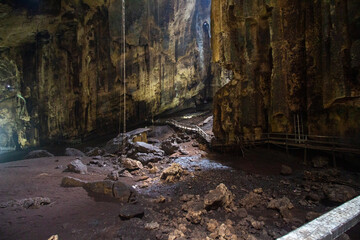 A mysterious and vast cavern with a walkway and natural light filtering in from above.