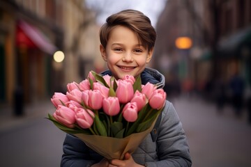 Fototapeta premium A boy smiling and holding a bouquet of pink tulips. The concept of March 8. Women's Day