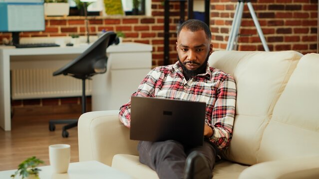 Easy going african american employee working from home on laptop, Teleworker remotely doing various tasks, typing on keyboard in stylish cozy warm apartment personal office