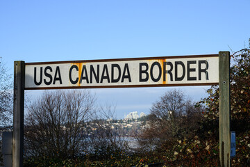 Text sign in black capital letters on white background for USA Canada Border with rust marks from metal frame