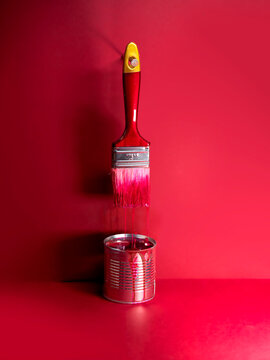 Red paintbrush hanging over a tin of red paint against a red background