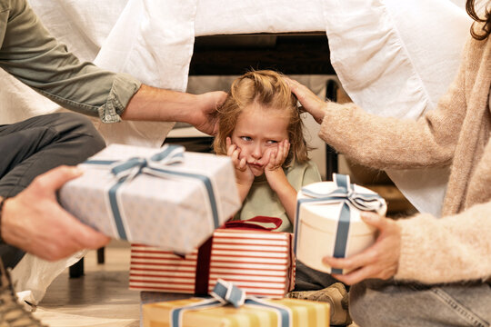 Two Parents sitting on the floor giving gifts to their unhappy son