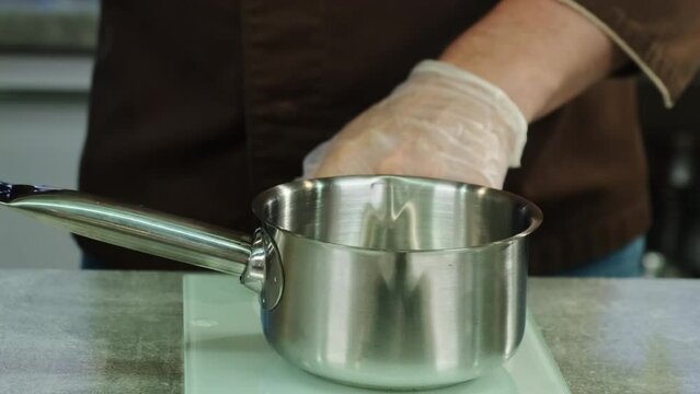 Professional cook places saucepan on scale measuring required amount of juice. Male culinarian measures correct quantity of ingredient