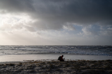 Photographer at the beach of a coast during a gale from the west. Breaking waves in the background