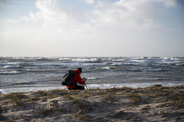 Photographer at the beach of a coast during a gale from the west. Breaking waves in the background