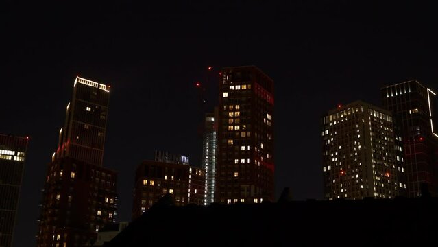 TIME LAPSE: Beautiful cityscape with business and residential buildings in the late evening hours. Lit lights shine through windows of tall urban skyscrapers in London district under dark night sky.