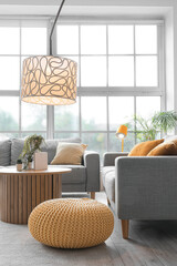 Interior of light living room with cozy grey sofas, coffee table and glowing lamps near big window