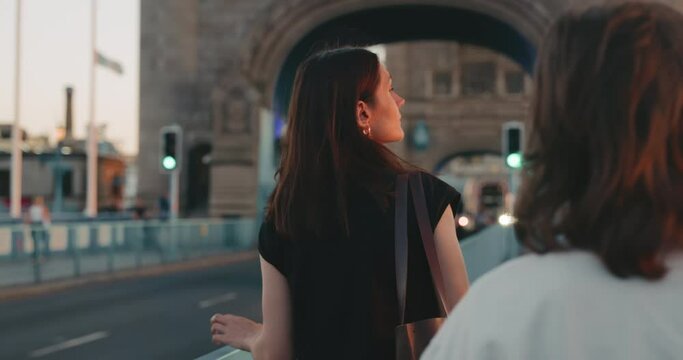 Beautiful young woman walks across Tower Bridge and turns sideways, illuminated by the beautiful setting sun