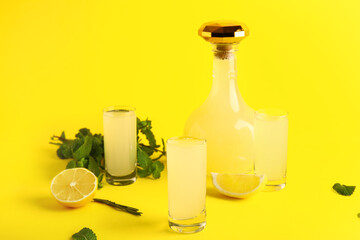 Bottle and shots of tasty Limoncello with mint on yellow background